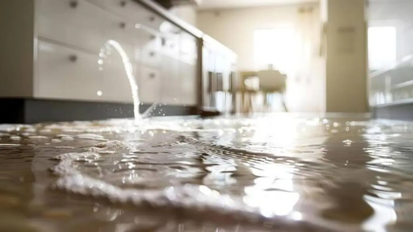 Water spreading across a kitchen floor in front of white cabinets